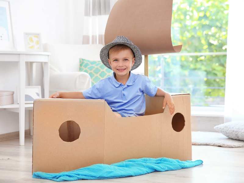 little-boy-playing-with-cardboard-ship-indoors