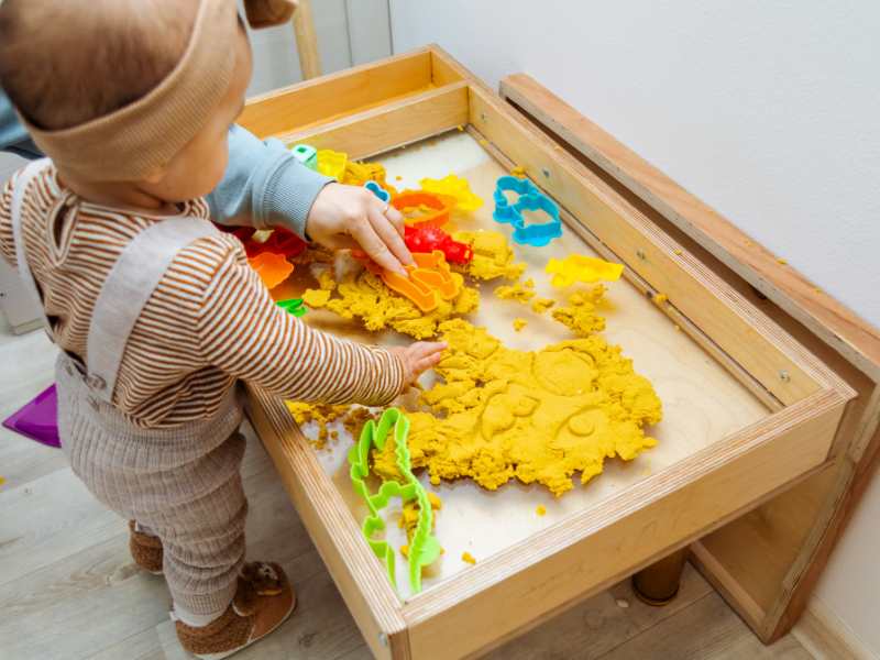 toddler-playing-with-kinetic-sand-with-plastic-shapes-on-sensory-tables