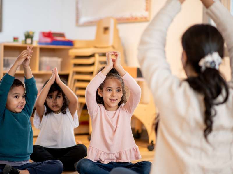 kids-sit-on-the-floor-with-their-hands-above-their-heads-practicing-yoga