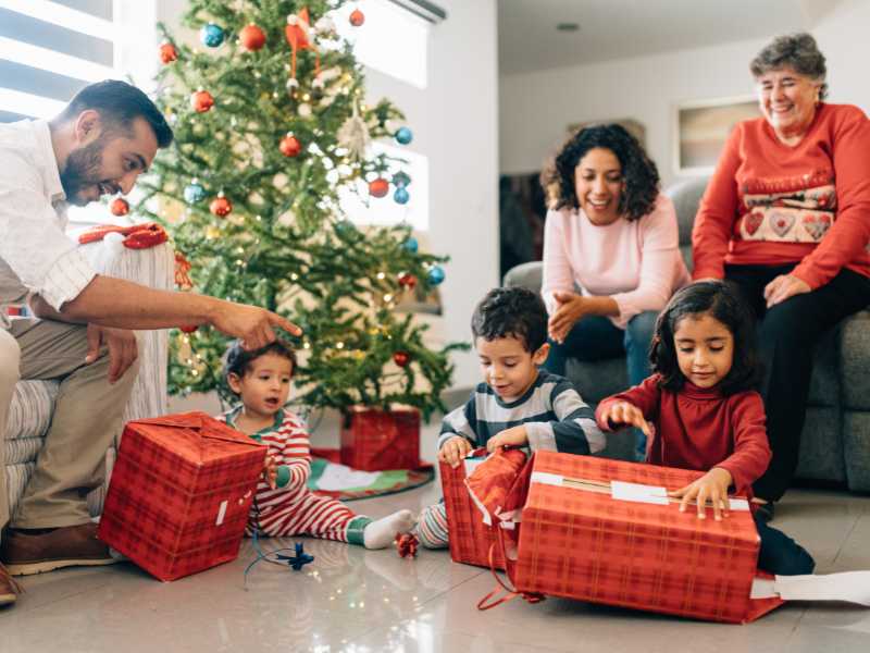 family-of-5-unwrapping-Christmas-gifts-with-a-large-Christmas-tree-by-the-side