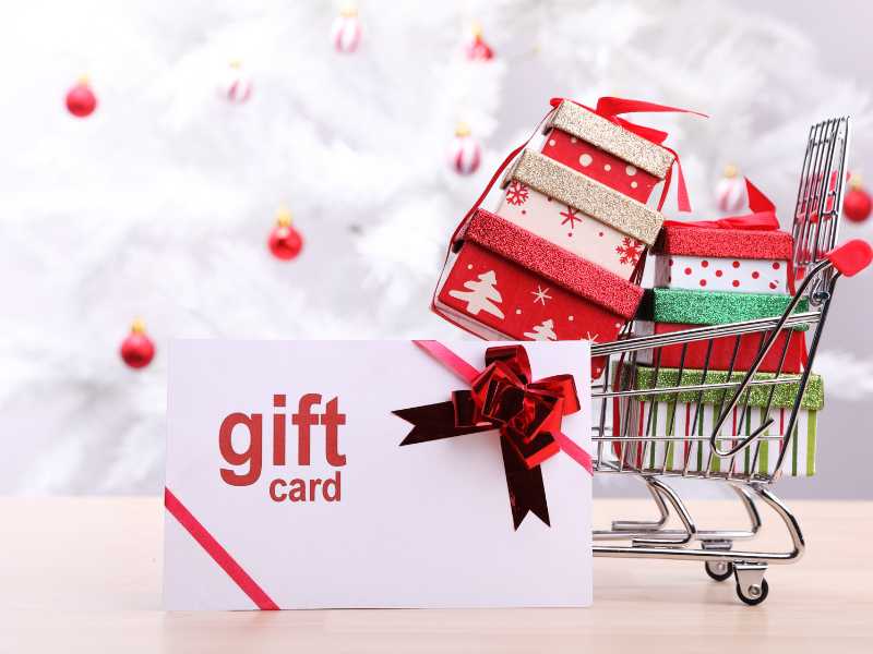 a-gift-card-next-to-a-shopping-cart-full-of-gift-boxes