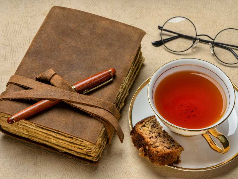 a-brown-leather-bound-journal-with-a-cup-of-tea-and-snack-and-eye-glass