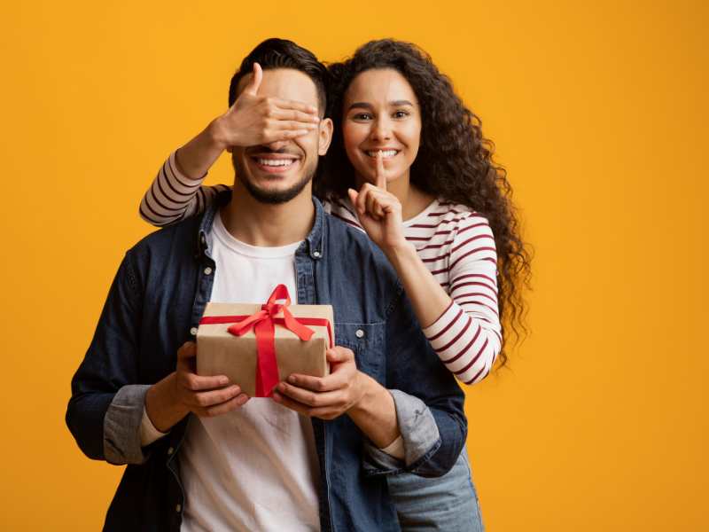 a-lady-covering-mans-face-with-palm-with-a-valentine-gift-for-boyfriend