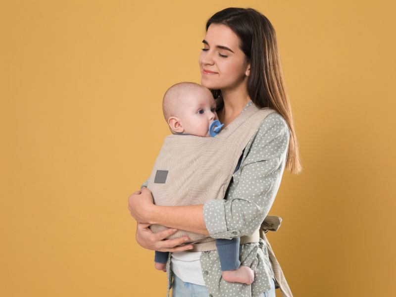 woman-carring-a-baby-with-a-wrap-in-front-on-a-yellow-background