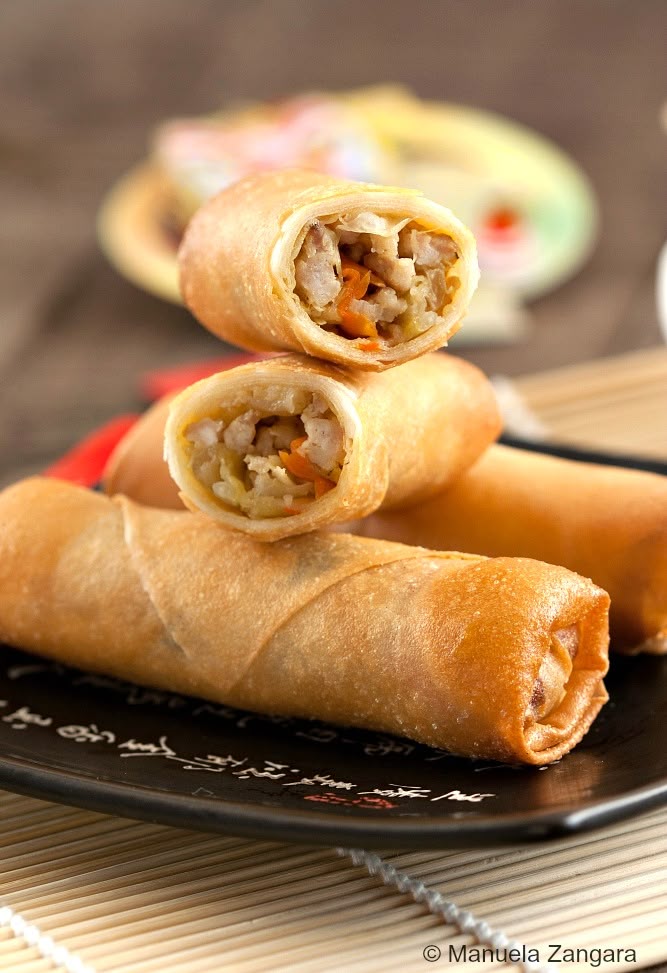 A-close-up-view-of-three-golden-brown-spring-rolls-on-a-black-plate-with-white-asian-style-script