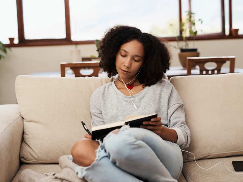 young-woman-writing-on-a-notebook-on-the-sofa-at-home