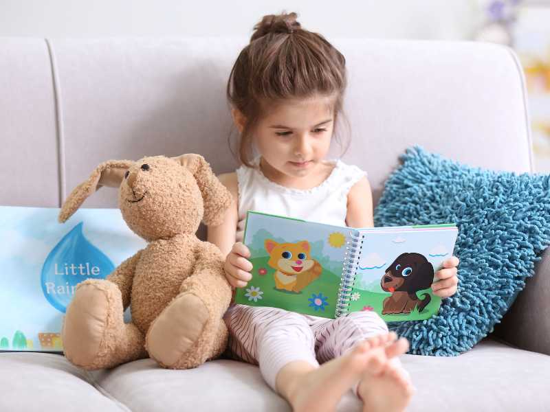 little-girl-reading-sticker-book-on-the-bed-with-bunny-on-easter-season