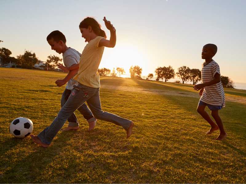 children-kicking-ball-in-outdoor-game-for-spring-parties