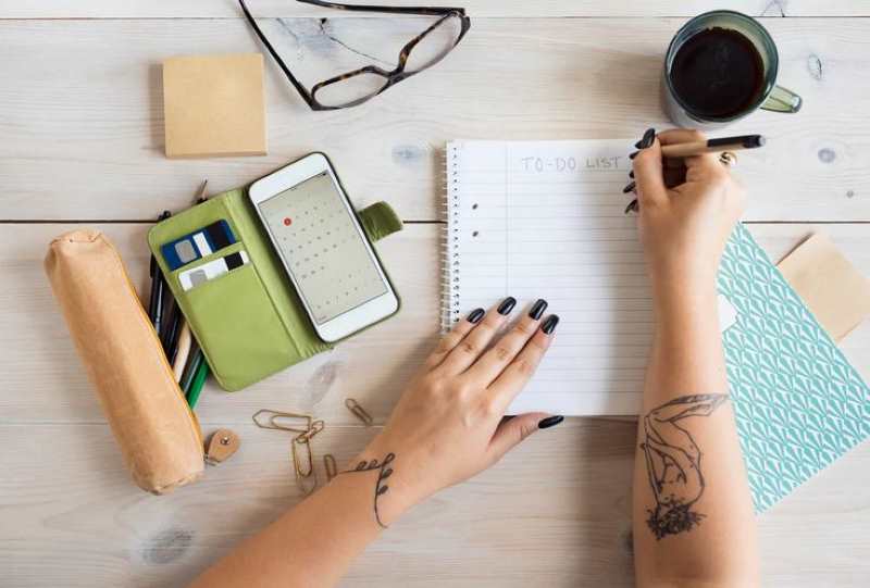 hand-writing-on-a-white-paper-with-phones-and-lens-on-the-table