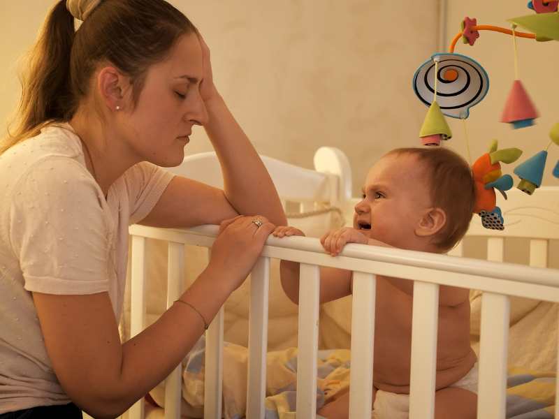 mom-feeling-exhausted-with-a-baby-in-the-crib